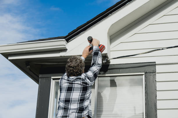 Person installing security camera on house exterior under blue sky