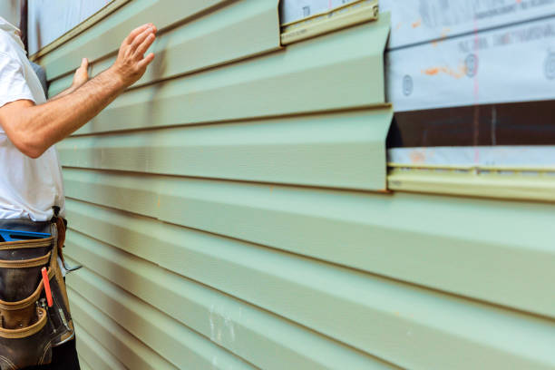 Worker installing light green vinyl siding on a house exterior