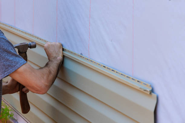 Worker installing vinyl siding on exterior of building with hammer