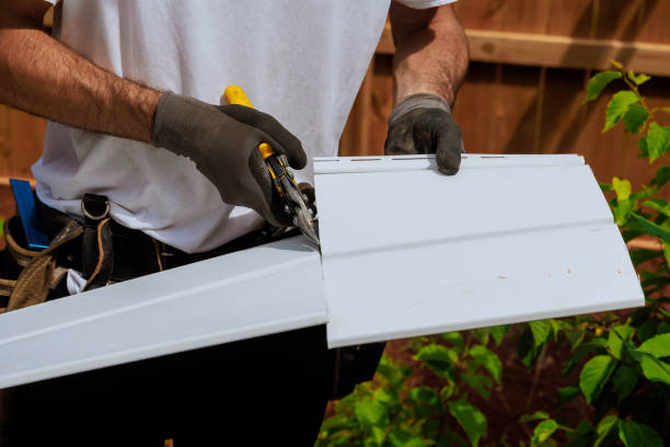 Worker in gloves installing white siding or trim on building exterior