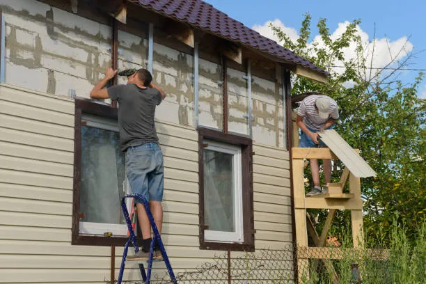 Two workers repairing and installing siding on a house exterior