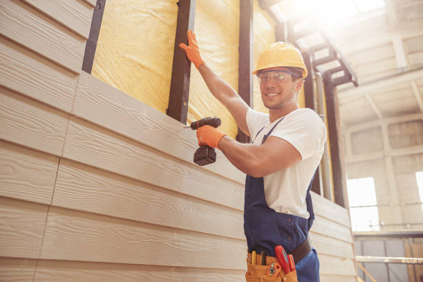 Construction worker installing siding on building with drill and safety gear