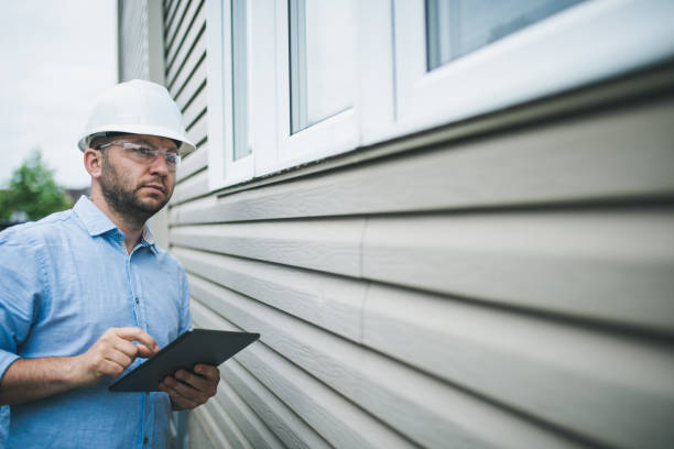 Construction worker in hard hat inspecting building exterior with tablet