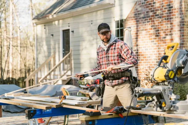 Carpenter working with power tools on wooden planks outside a house