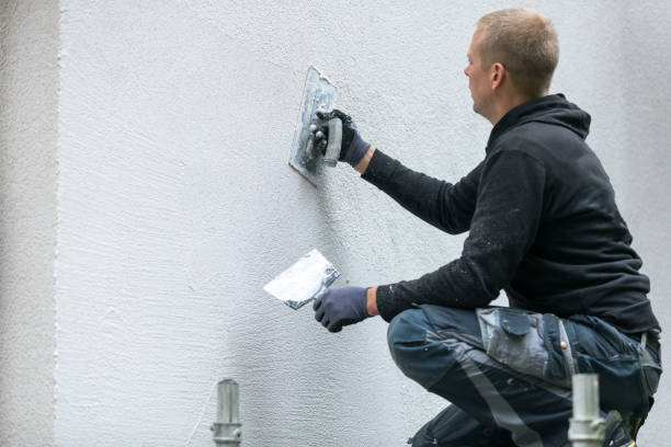 Worker smoothing wall surface with plastering tool, wearing work clothes
