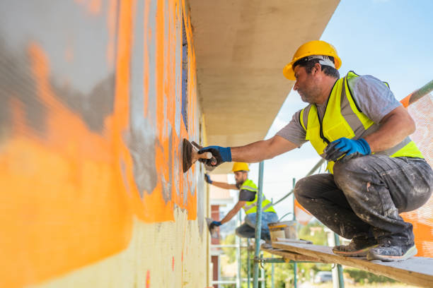 Construction worker painting wall in yellow safety gear on scaffolding