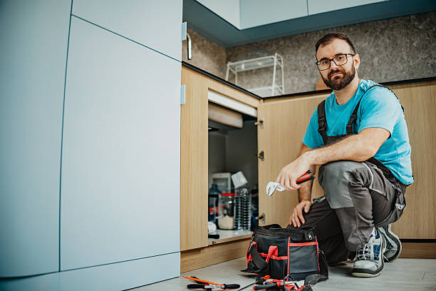 Maintenance worker crouching near toolbag, preparing to repair kitchen cabinet