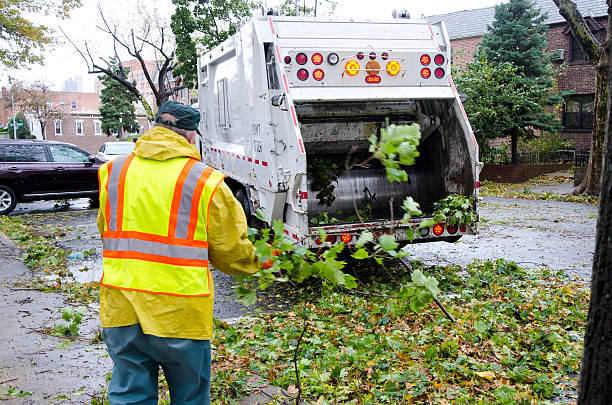 Waste collector in safety vest loading tree branches into garbage truck