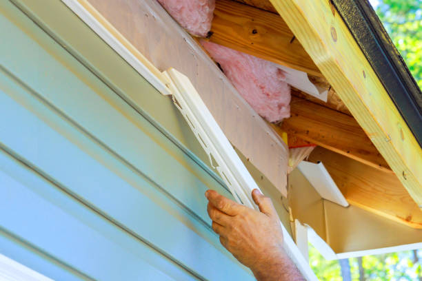Worker installing siding and insulation on house exterior roof edge