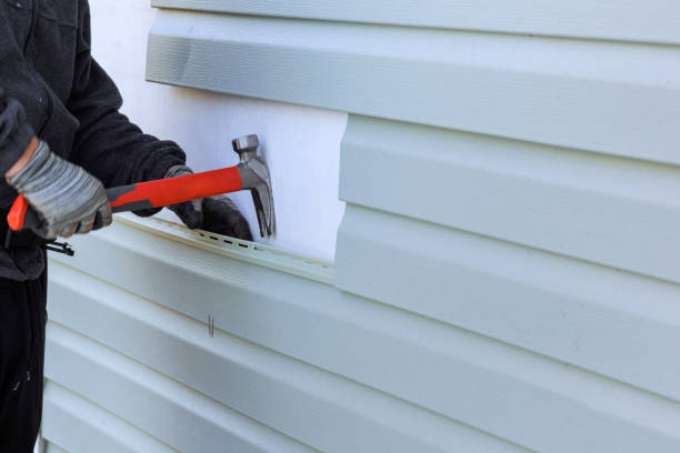 Worker installing vinyl siding with hammer on white exterior wall