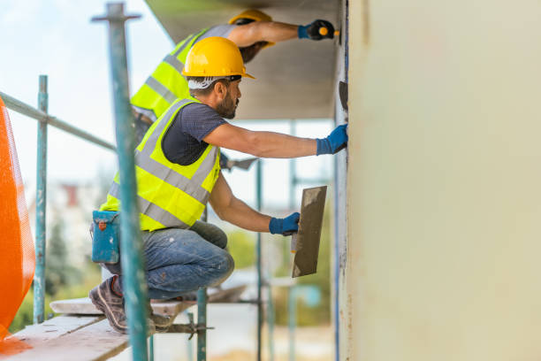 Construction worker in safety vest and hard hat plastering wall on scaffolding