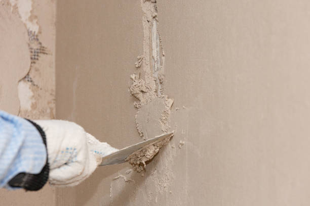 Gloved hand using putty knife to repair damaged wall surface