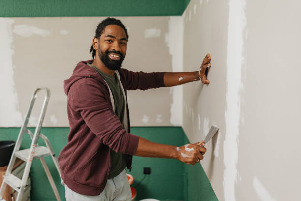 Smiling person painting wall green and white with roller and ladder