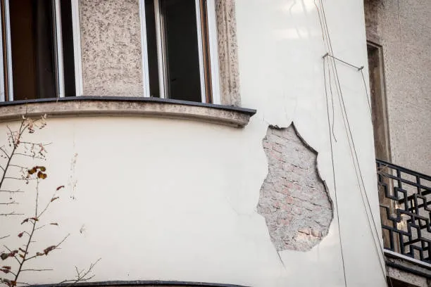 Damaged white wall with cracked plaster revealing underlying brick texture
