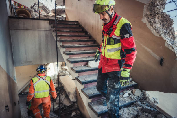 Rescue workers in safety gear inspect damaged staircase after building collapse