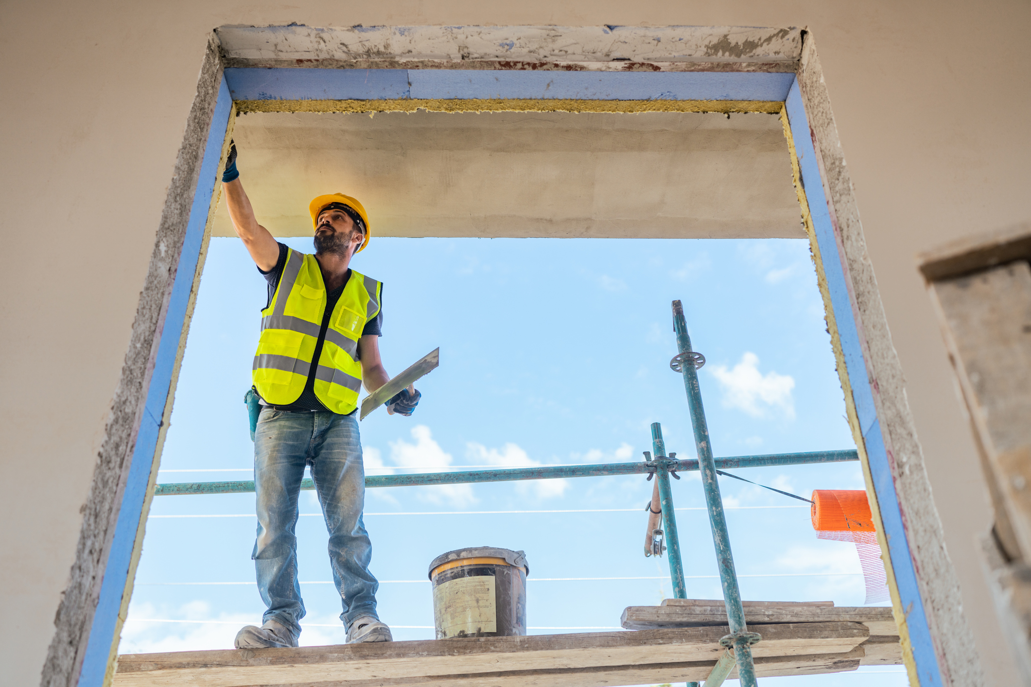 Construction worker in safety vest and hard hat standing on scaffolding
