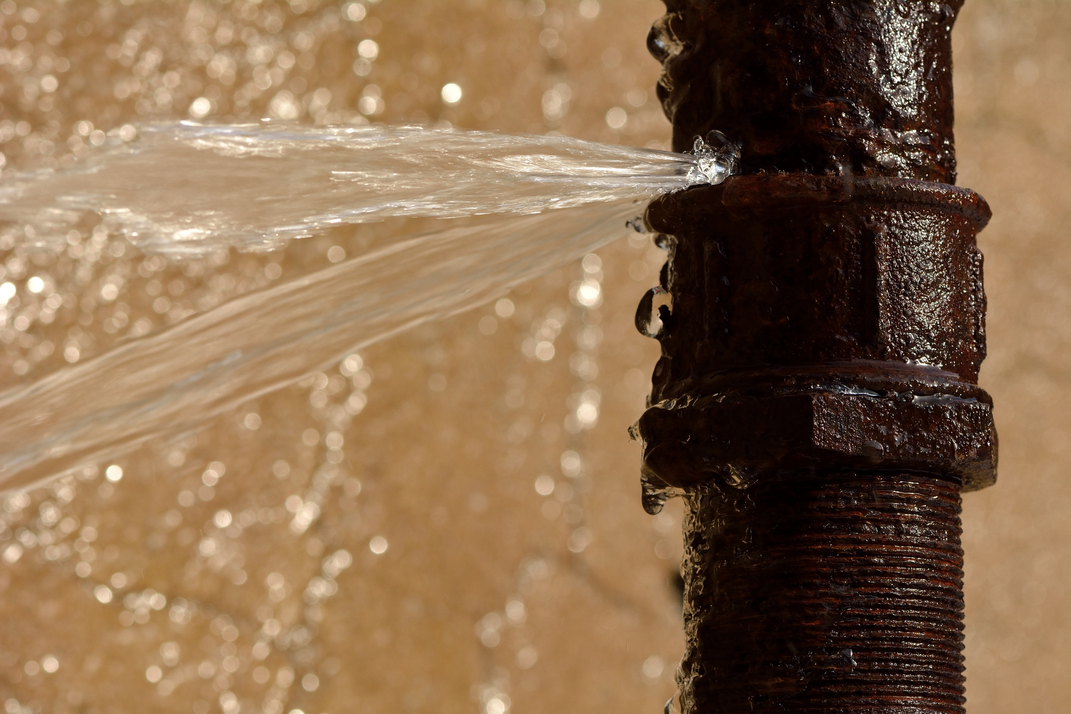 Water spraying from a rusty metal pipe with golden bokeh background
