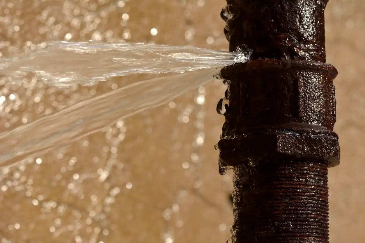 Water spraying from a rusted metal pipe with blurred golden background