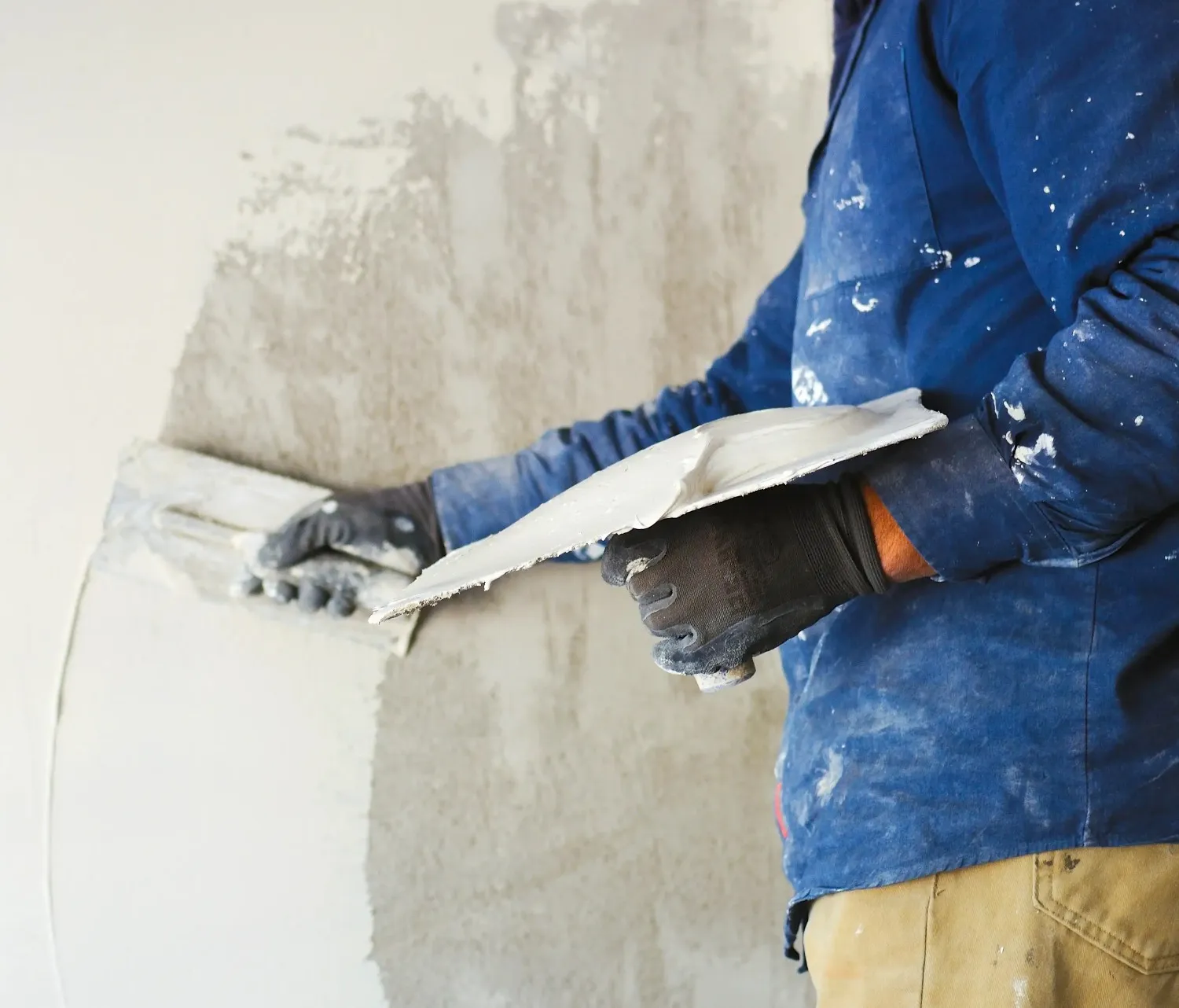 Construction worker smoothing wall with plastering trowel in white helmet