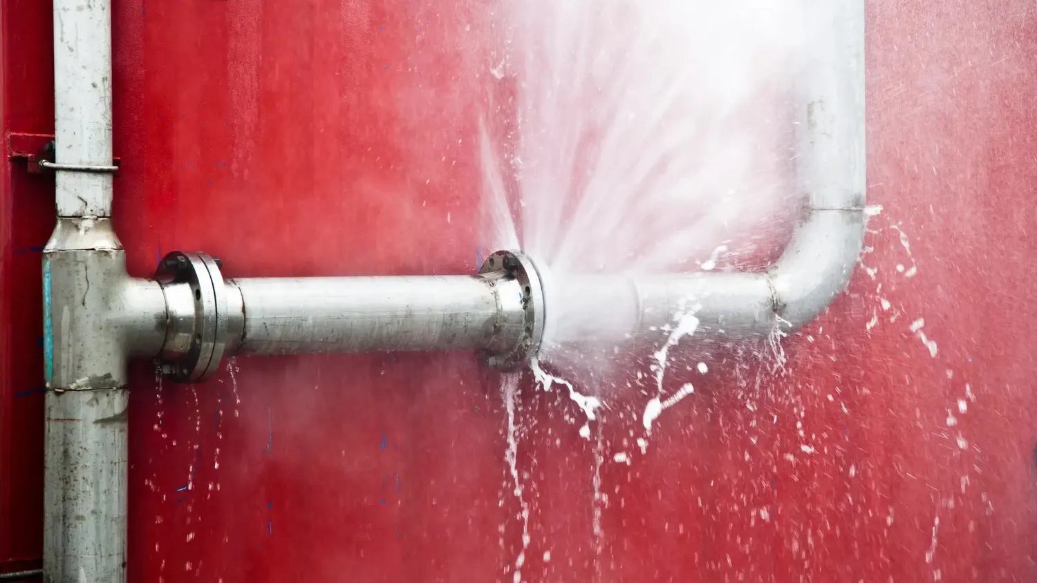 Water bursting from a damaged pipe with spray and droplets
