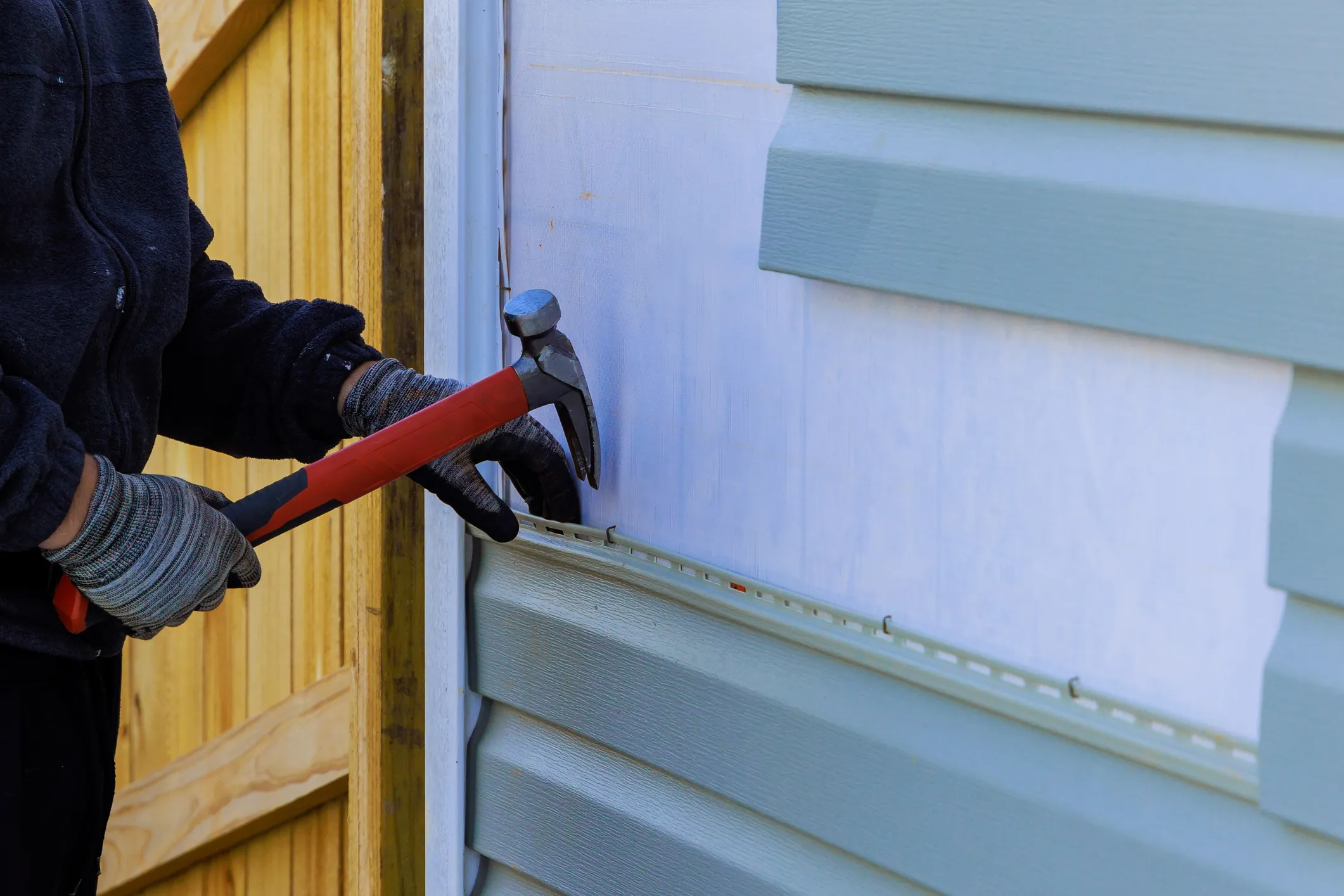 Gloved hand using hammer to install siding on a house exterior