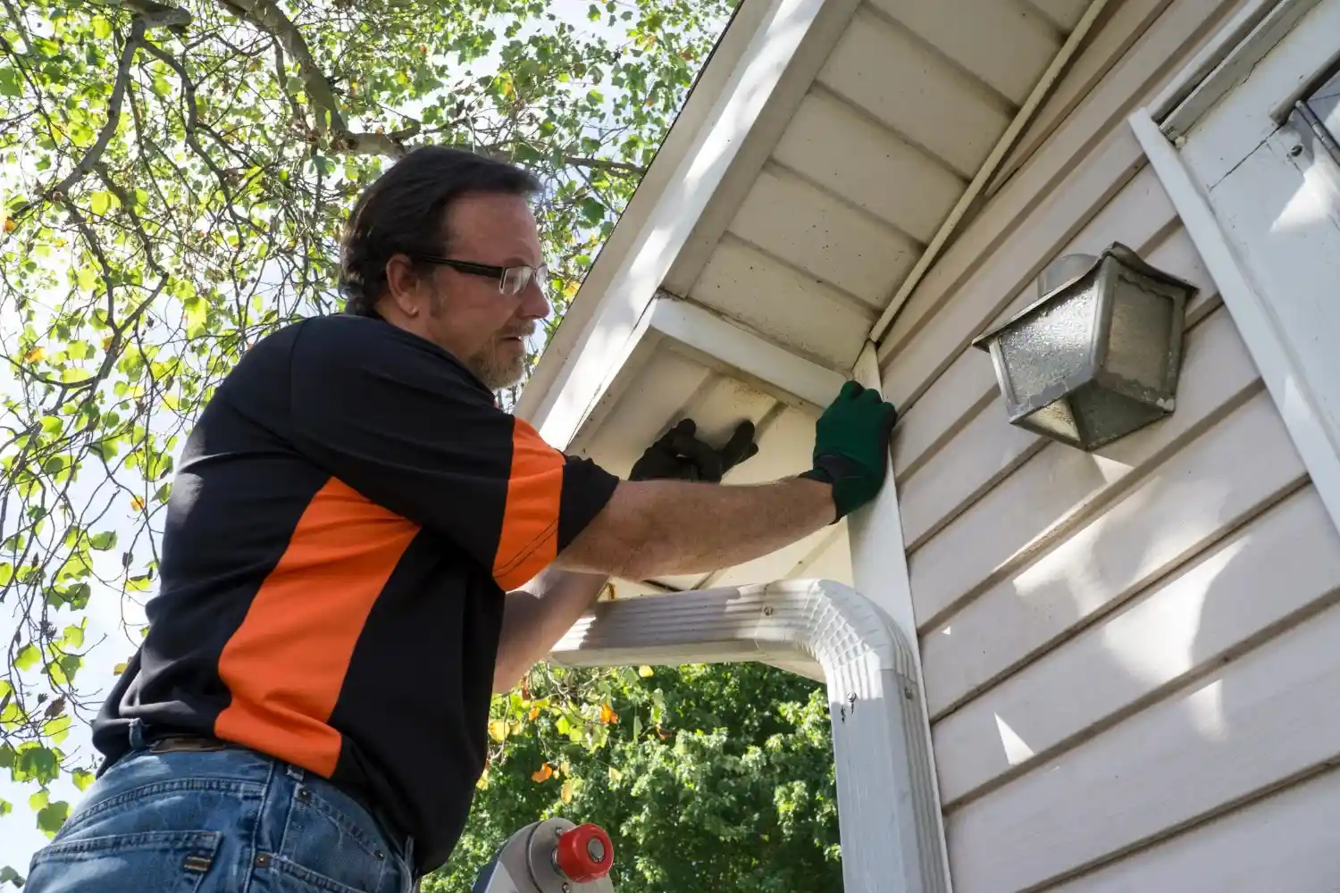 Worker in orange and black shirt installing outdoor light fixture