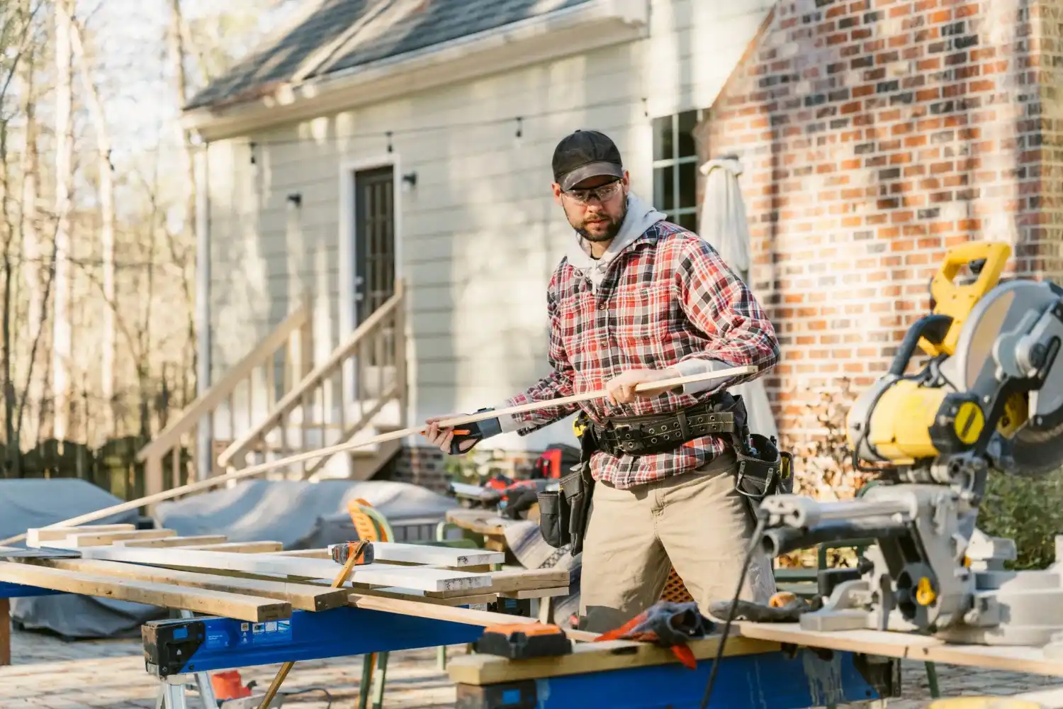 Carpenter working with power tools on wooden planks outside a house