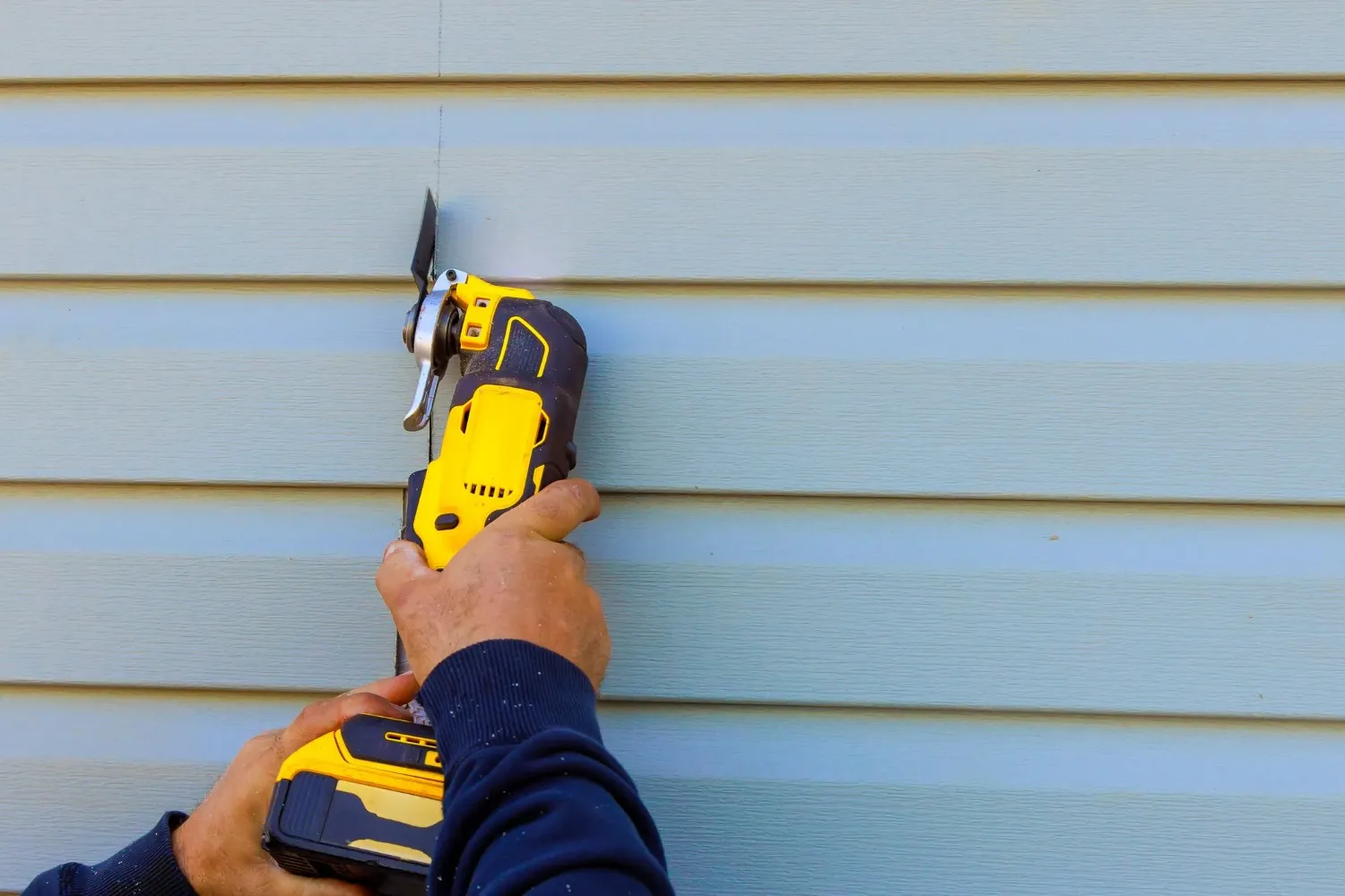 Yellow power drill being used on light blue horizontal siding panels