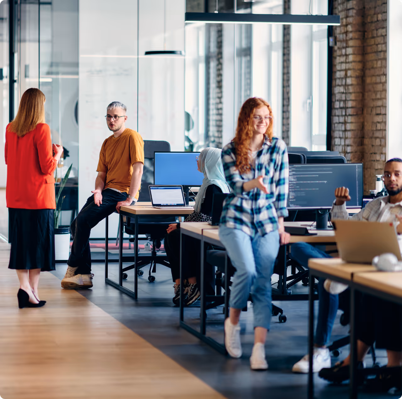 Modern office with diverse young professionals collaborating and working at computers in an open workspace.