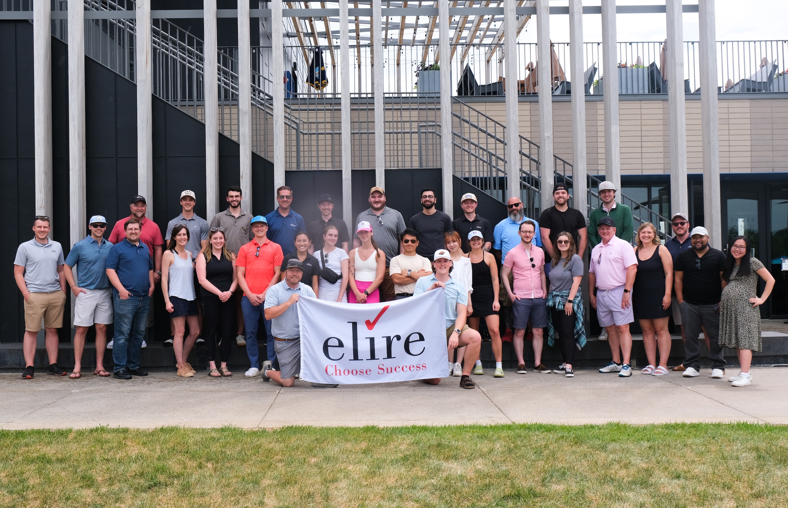 large group of people outside in exercise clothes holding a large white banner with the elire logo on it