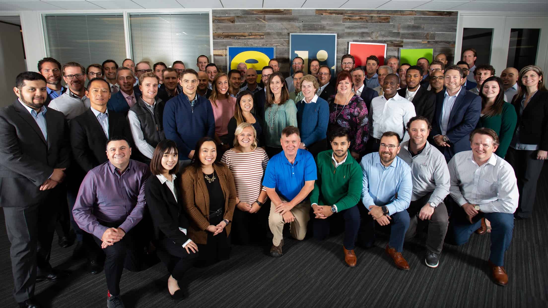 a large group of people all standing or on one knee in front of a sign that says "Elire" in the Elire office