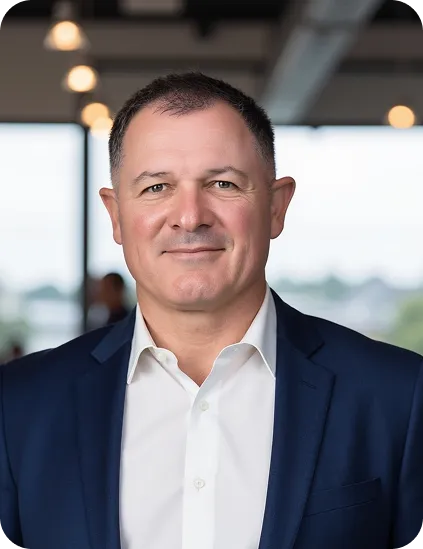 Smiling man wearing a white shirt and navy suit jacket in a modern office setting.