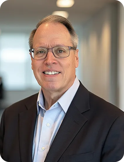 Smiling middle-aged man wearing glasses, a light blue shirt, and a dark blazer indoors.