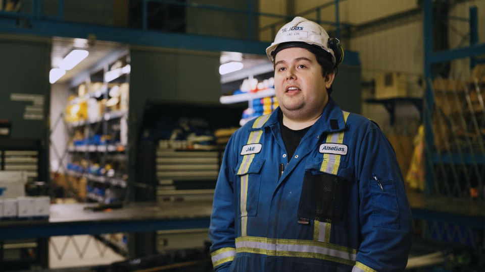 Man wearing a safety helmet and blue work uniform with reflective stripes standing inside an industrial warehouse.