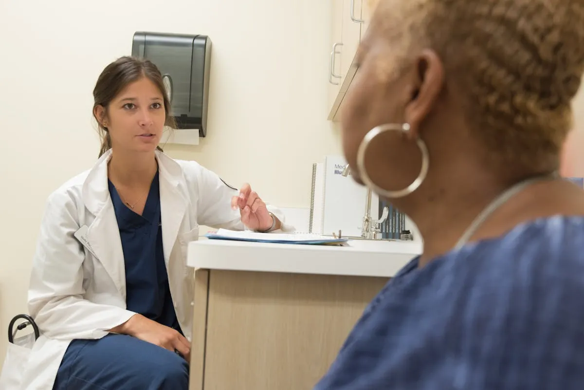 Female doctor in white coat speaking with a patient in a medical consultation room.