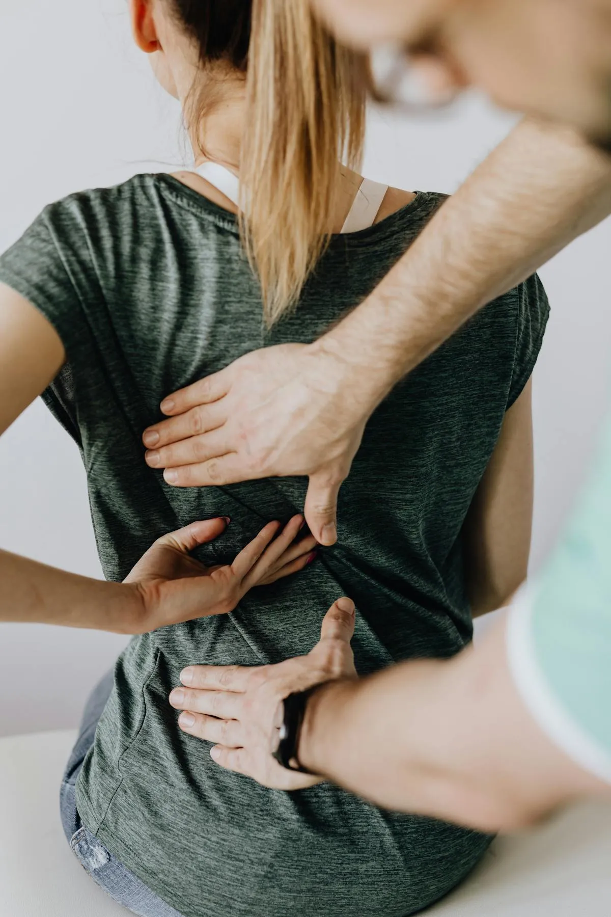 Chiropractor examining a woman's lower back with hands pressing on her spine.