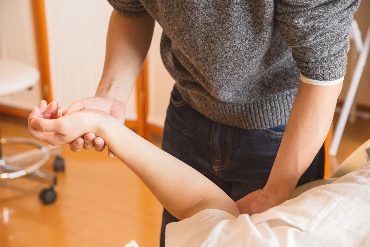 Chiropractor wearing gray sweater manipulating a patient's arm in a clinic.