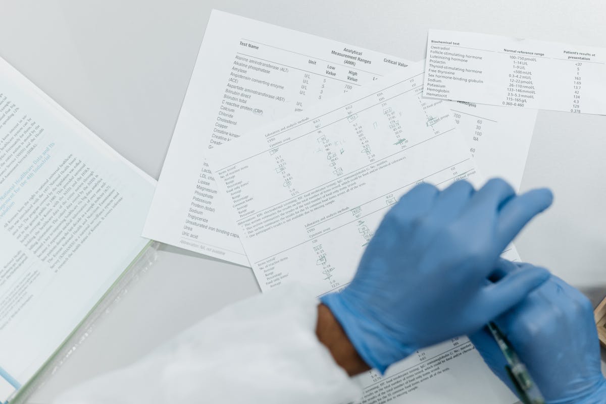 Person wearing blue gloves reviewing printed medical lab test results and reference ranges on a white table.