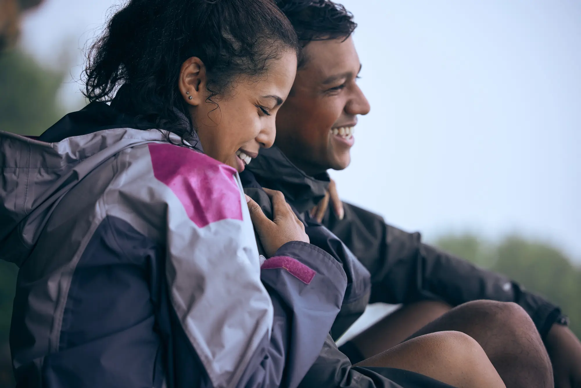 A candid shot of an affectionate couple, bundled up in colorful outdoor gear, sharing a joyful moment.