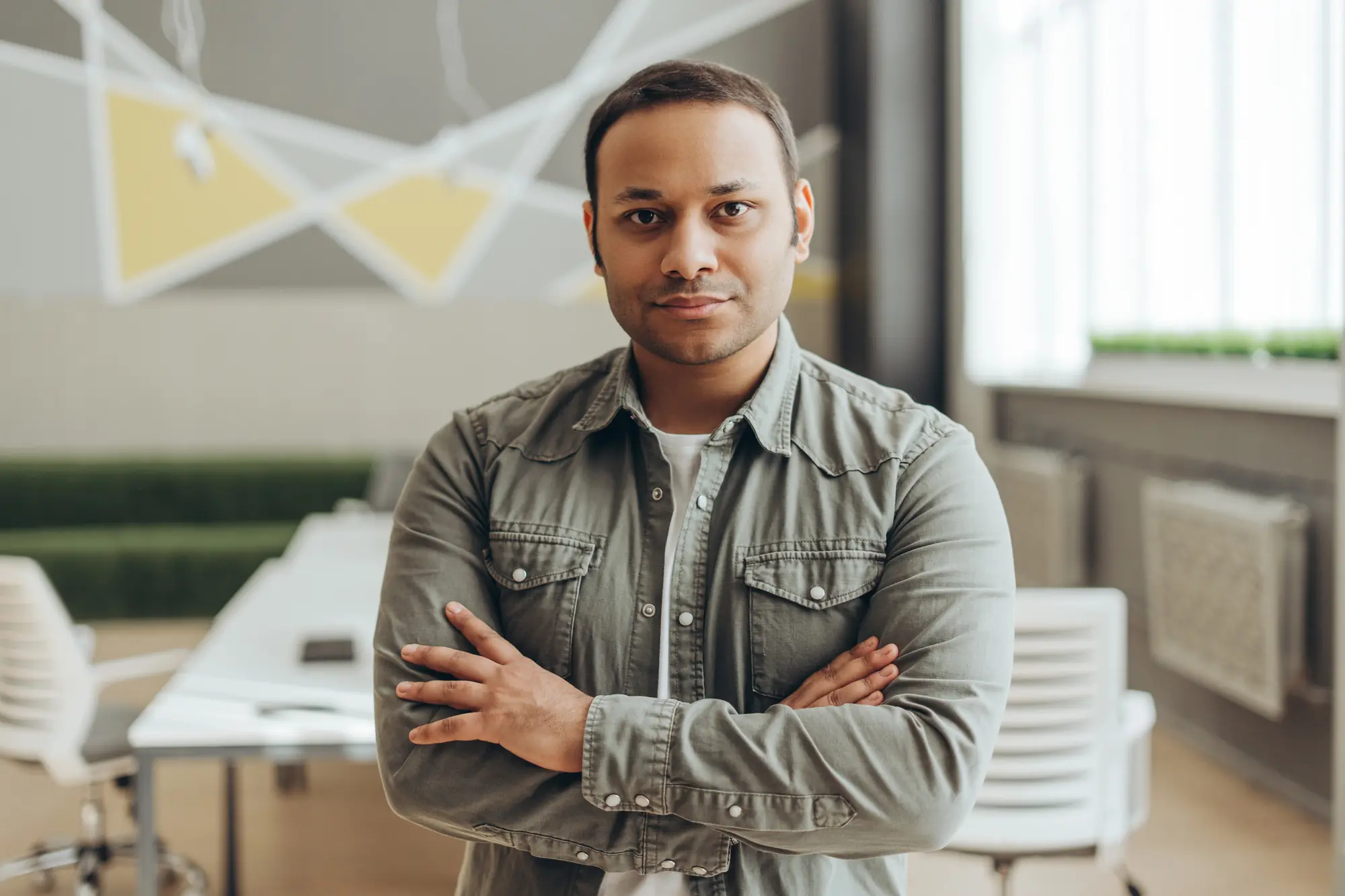 A man with crossed arms standing confidently in a modern office.

