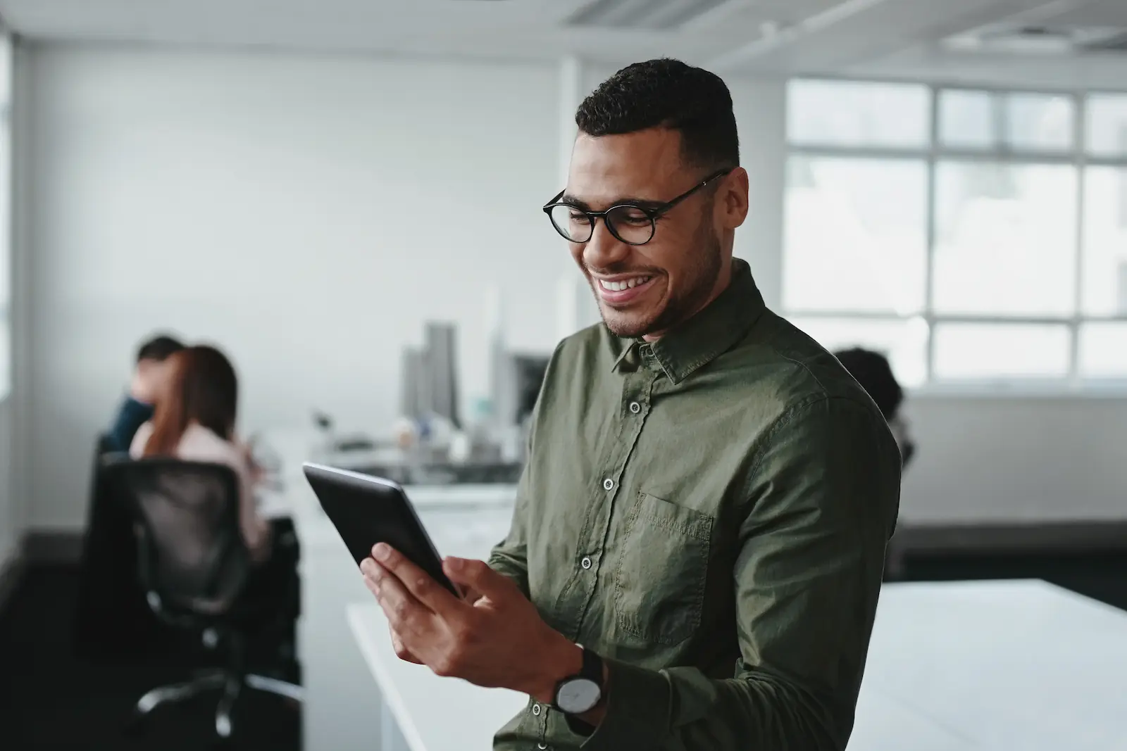 A young man in an office, smiling while looking at a digital tablet.