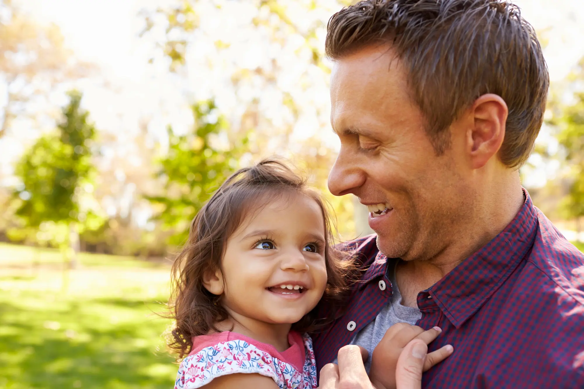 A smiling father holding his happy young daughter outdoors.
