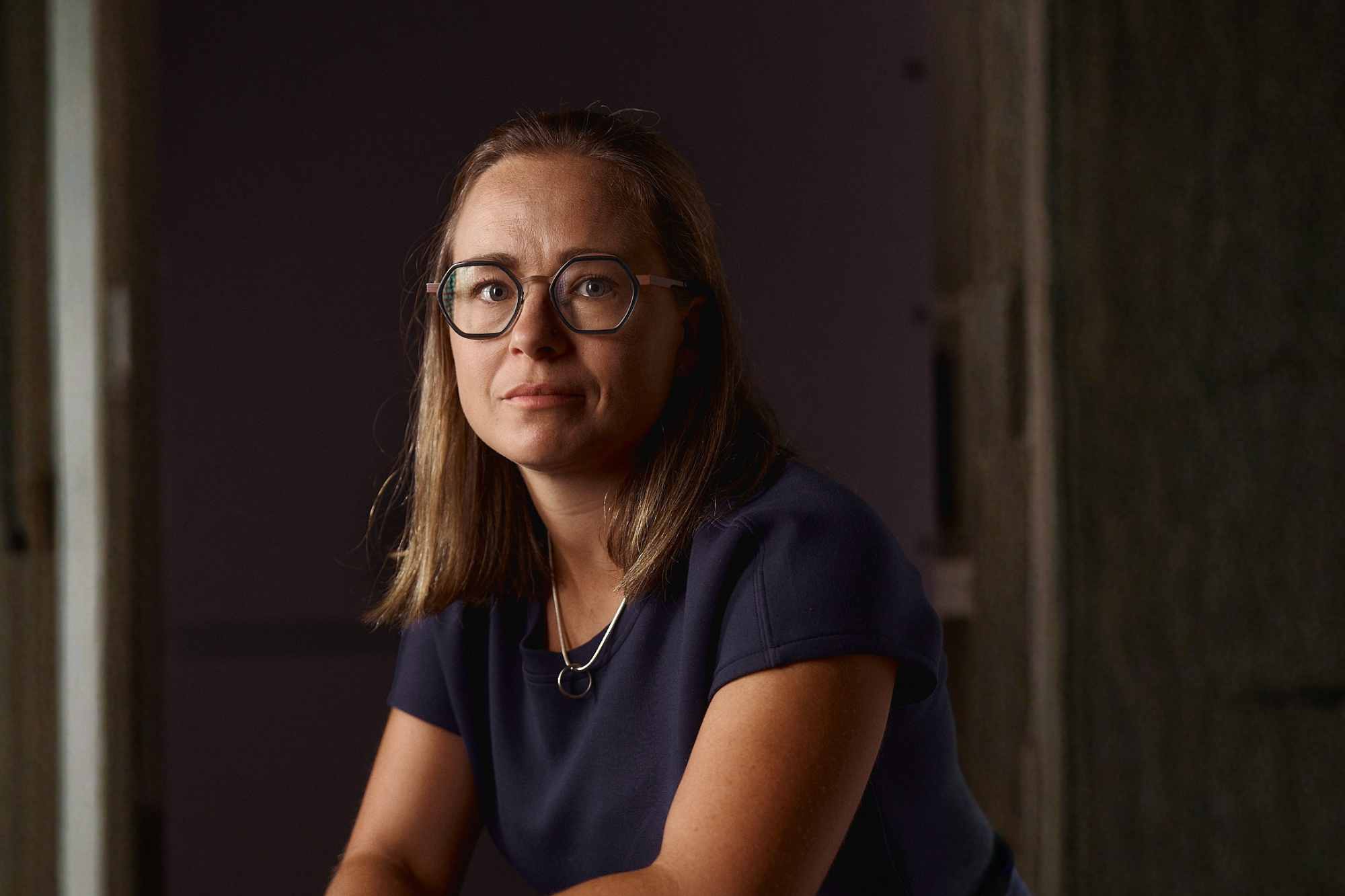 Woman with glasses and shoulder-length hair in a navy top, in a studio portrait