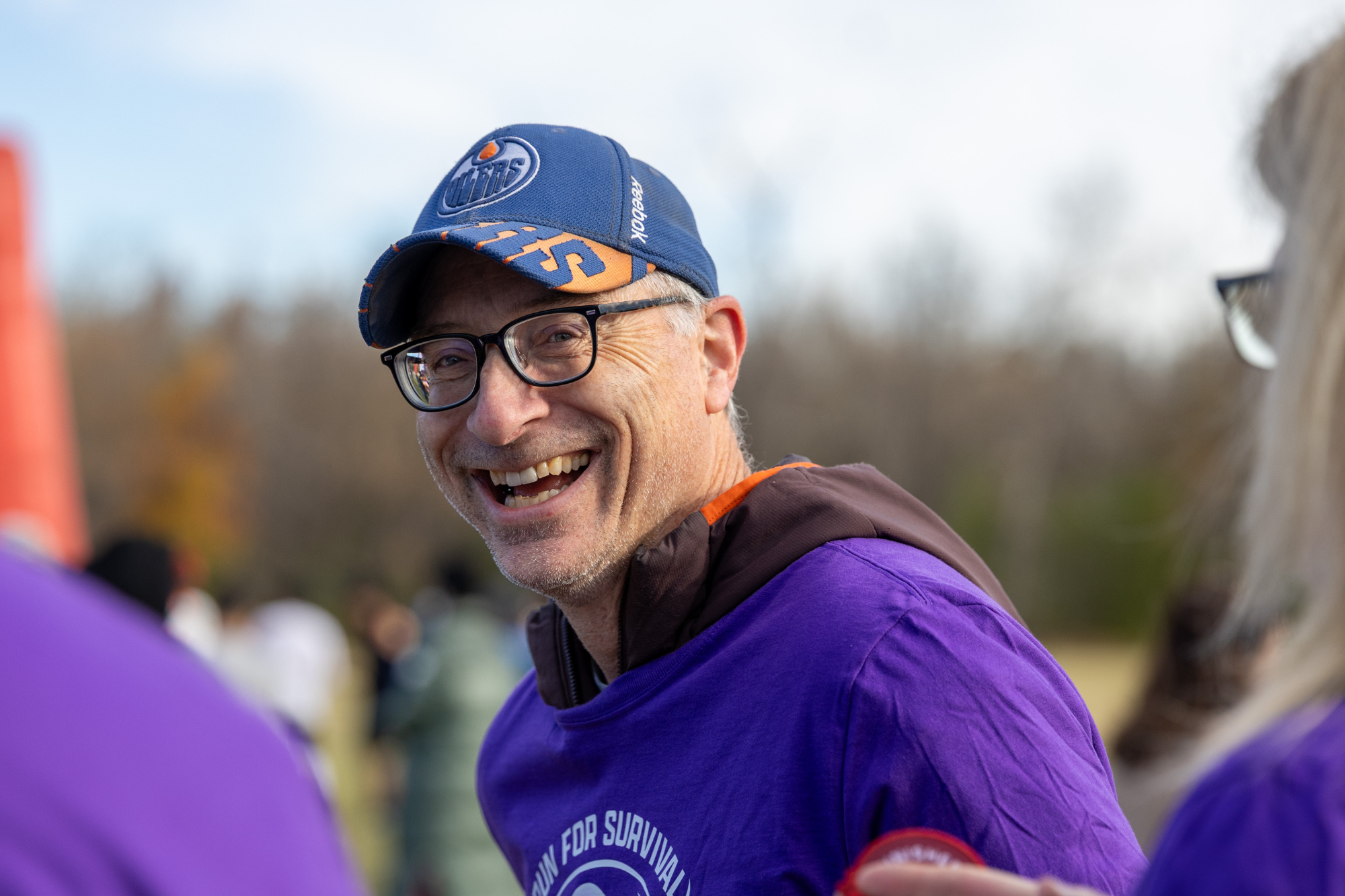 Smiling man in an Edmonton Oilers cap and purple event T-shirt at an outdoor fundraising walk