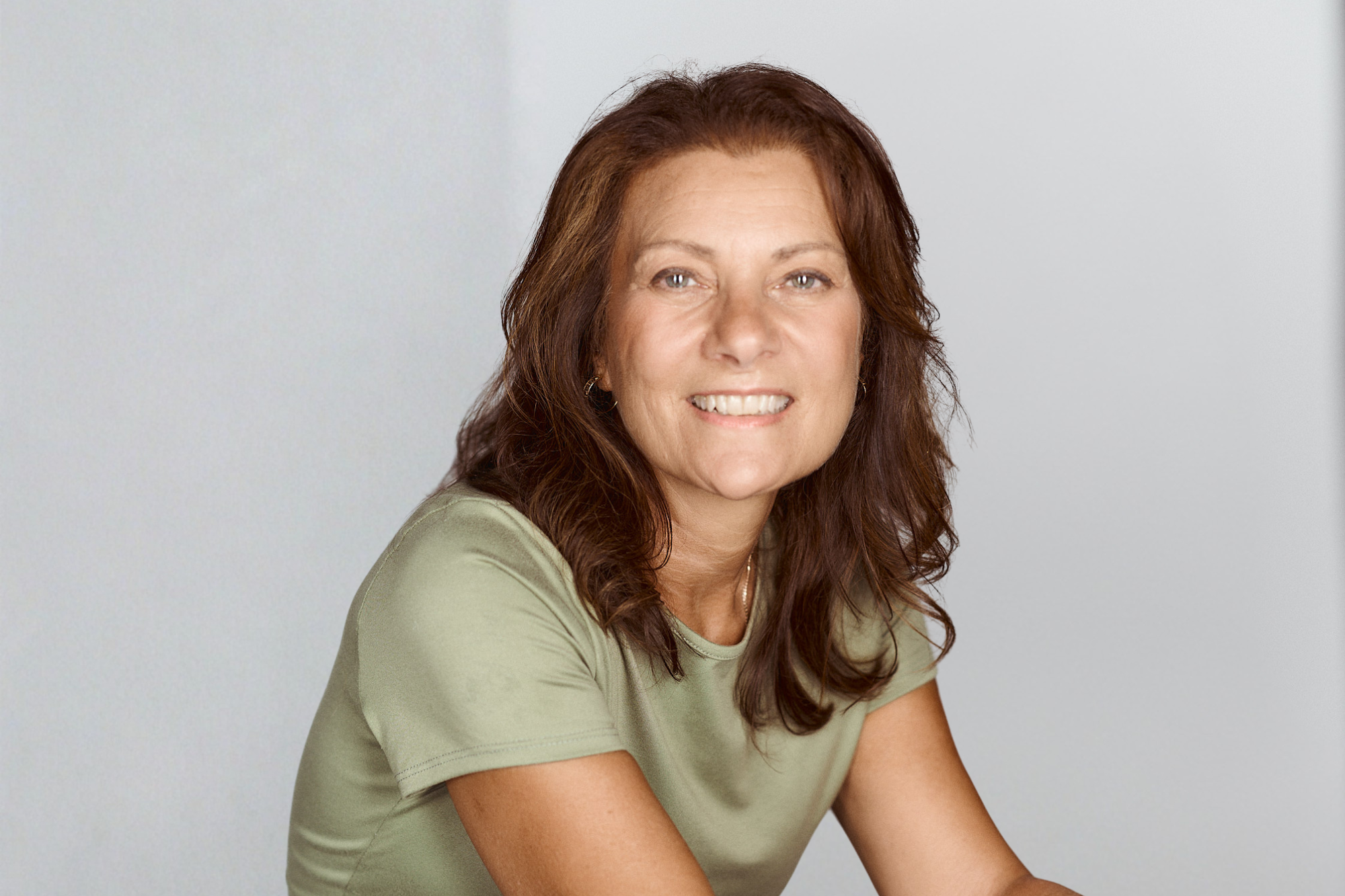 Smiling woman with long auburn hair in a sage green T-shirt