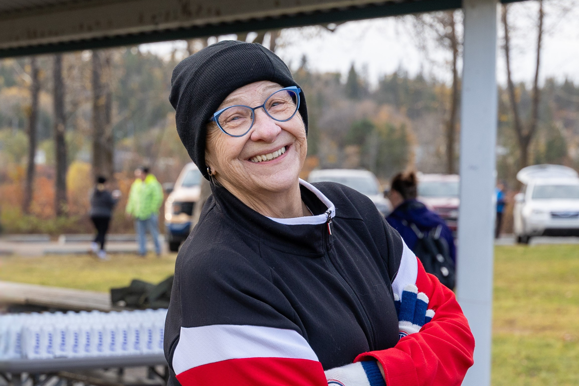 Smiling older woman in a black knit hat and glasses at an outdoor event