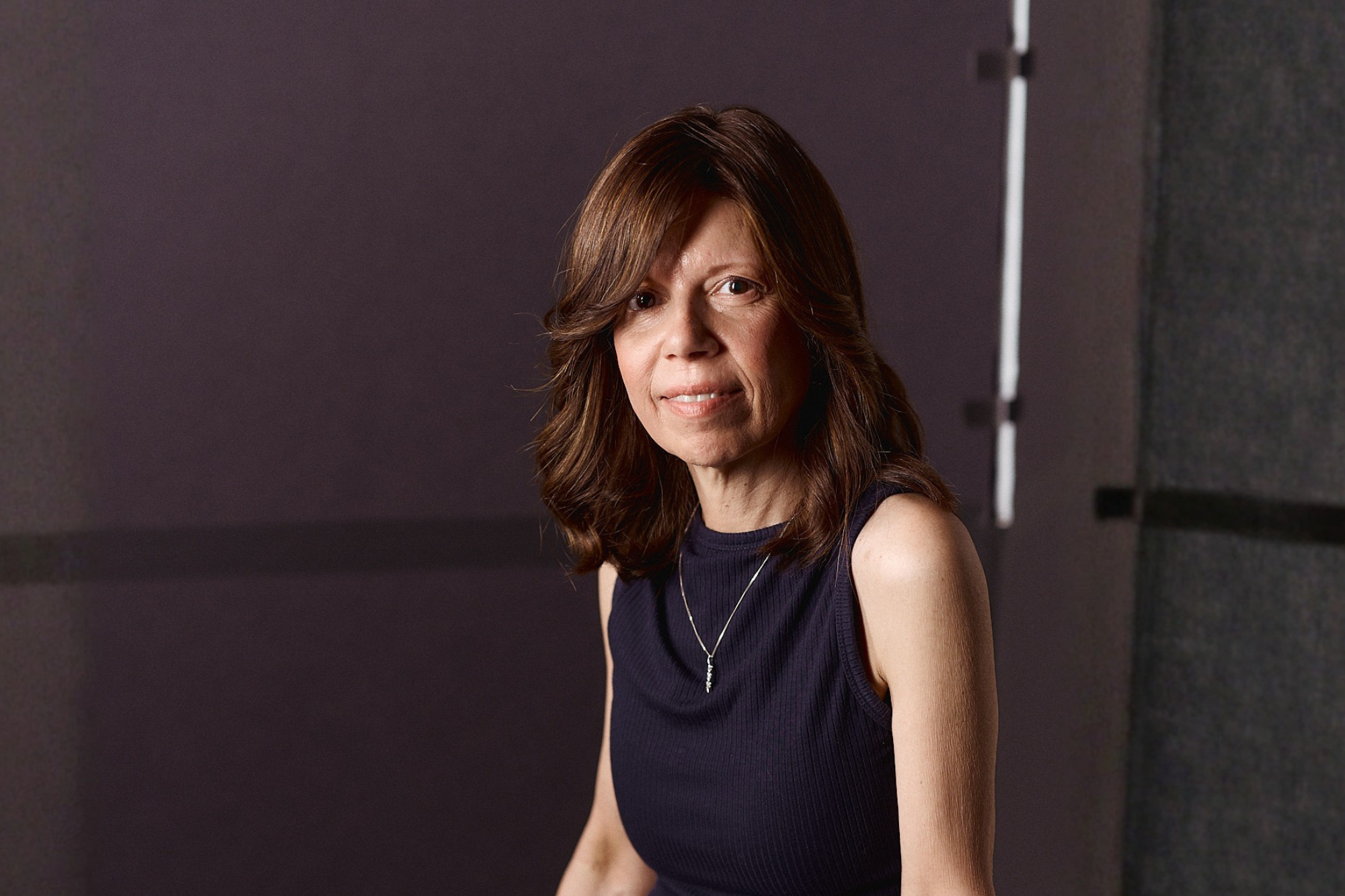 Woman with shoulder-length auburn hair in a sleeveless navy top, in a studio portrait