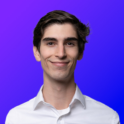 Young man with dark hair wearing a white collared shirt smiling against a blue gradient background.