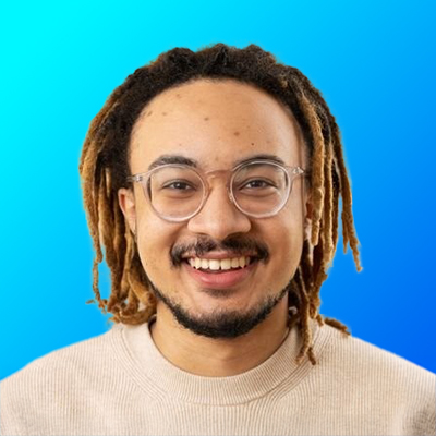 Smiling young man with glasses and dreadlocks wearing a light beige sweater against a bright blue gradient background.