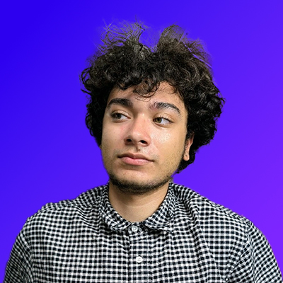 Young man with curly dark hair wearing a black and white checkered shirt against a blue-purple gradient background.